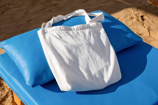 Mockup shopper handbag on blue lounger, beach sand background. Top view copy space shopping eco reusable bag.