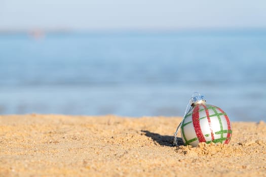 celebrating Christmas in hot countries. Christmas decorations bauble ball on sandy beach with sea background. copy space