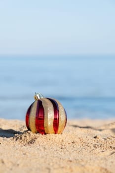 celebrating Christmas in hot countries. Christmas decorations bauble ball on sandy beach with sea background. copy space