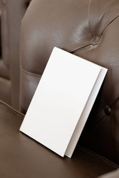 Book with blank cover on brown leather couch