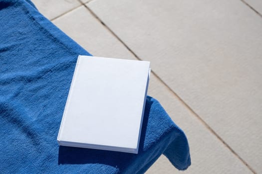 reading at vacation. blank book for mockup design on lounger by the swimming pool