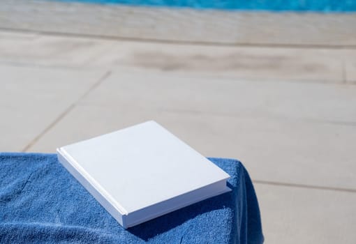 reading at vacation. blank book for mockup design on lounger by the swimming pool