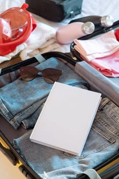 Travel concept. opened packed suitcase on bed in hotel room, blank book mockup