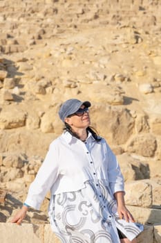 mature adult woman traveler wearing light colour clothing, facing the Pyramids of Gyza