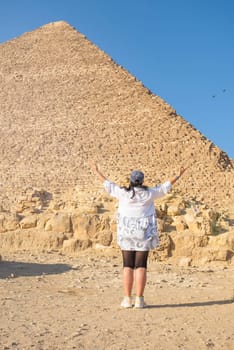 mature adult woman traveler wearing light colour clothing, facing the Pyramids of Gyza