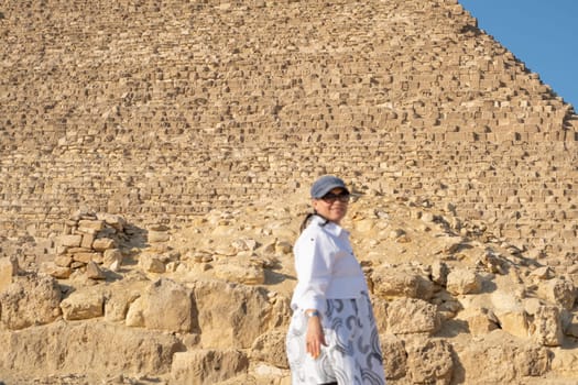 mature adult woman traveler wearing light colour clothing, facing the Pyramids of Gyza