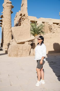 mature adult woman traveler explores the ruins of the ancient Karnak temple in the city of Luxor in Egypt. Great row of columns with carved hieroglyph