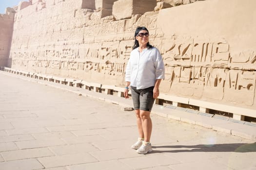 mature adult woman traveler explores the ruins of the ancient Karnak temple in the city of Luxor in Egypt. Great row of columns with carved hieroglyph