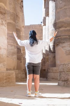 mature adult woman traveler explores the ruins of the ancient Karnak temple in the city of Luxor in Egypt. Great row of columns with carved hieroglyph