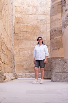 mature adult woman traveler explores the ruins of the ancient Karnak temple in the city of Luxor in Egypt. Great row of columns with carved hieroglyph