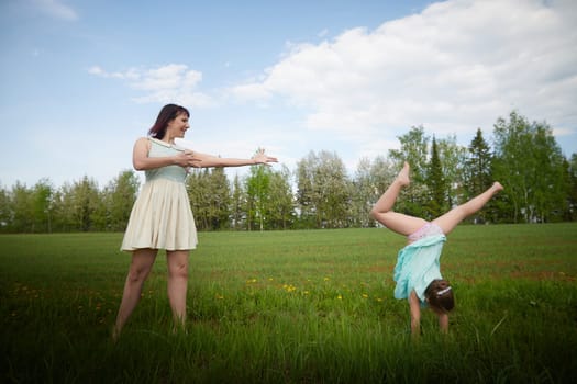 Happy mother and daughter enjoying rest, playing, fun and doing sports exercises on nature in a green field. Woman and girl resting outdoors in summer and spring day