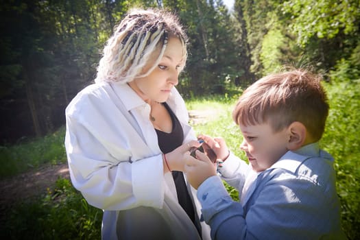 Young fat teenage boy playing with phone and mother swears, demands to stop it in a park. Blogger, gamer, streamer son online on Internet and conflict