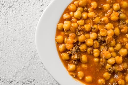 Chickpea stew with minced meat on a white porcelain plate on a stone table