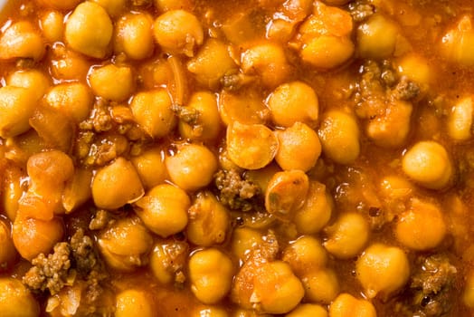 Chickpea stew with minced meat on a white porcelain plate on a stone table