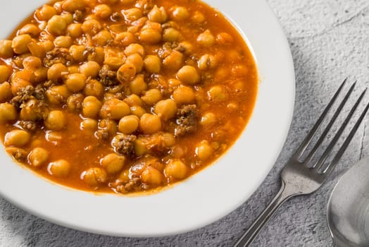 Chickpea stew with minced meat on a white porcelain plate on a stone table