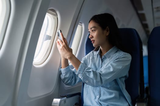 Asian people female person onboard, airplane window, using mobile while on the plane.