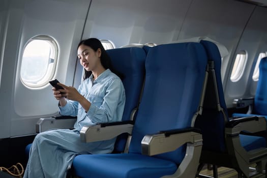 Asian people female person onboard, airplane window, using mobile while on the plane.