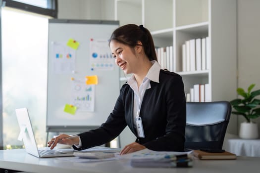 Charming Asian business woman sitting working on laptop in office.