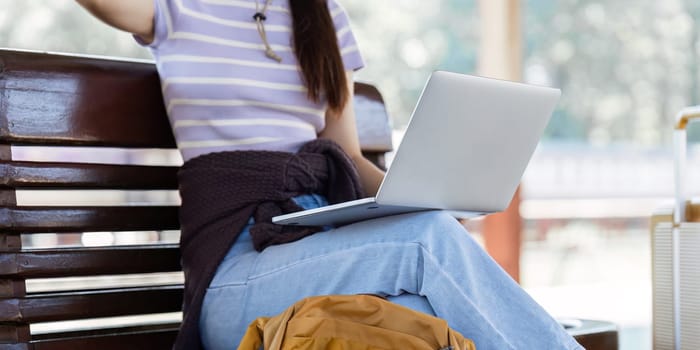 Woman traveler with backpack using laptop to planning vacation on holiday relaxation at the train station.