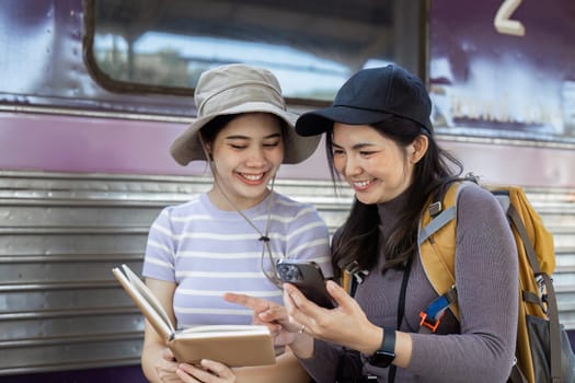 two women traveler friends are at the train station checking the map of the city on mobile.