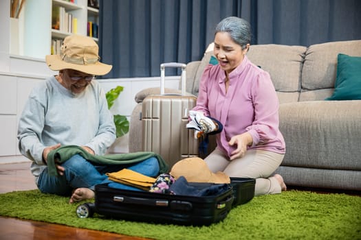 Asian couple old senior marry retired couple smiling prepare luggage suitcase arranging for travel, Romantic mature retired packing clothes travel bag suitcase together on floor at home for holiday
