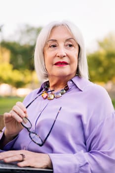 portrait of a senior woman sitting in the park with her glasses in her hand, concept of elderly people leisure