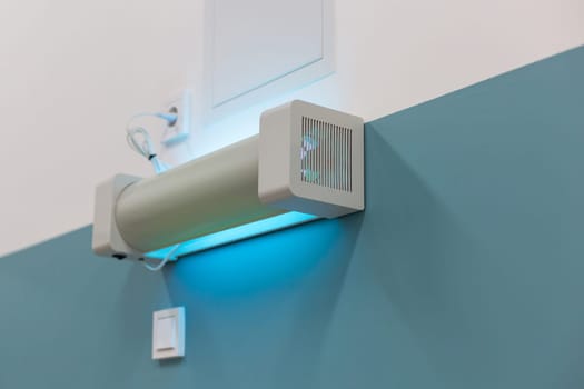 Wall-mounted UV sterilization lamp emitting blue light for disinfection in a hospital setting