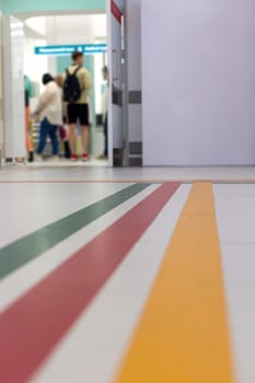 Colorful guide lines: green, red, yellow, on the floor of the hospital corridor for navigation, with blurred figures of visitors in the background