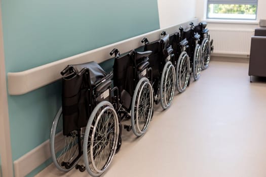 A row of empty folded wheelchairs along a corridor of clinic .