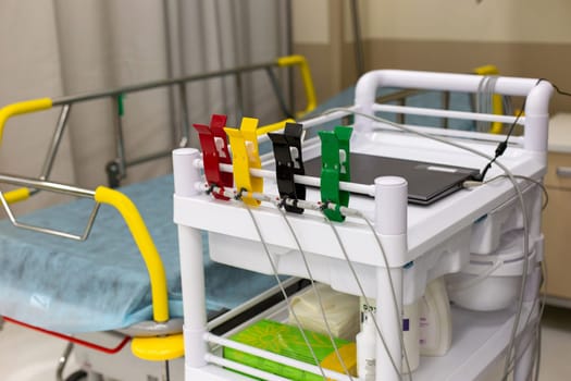 Multi-colored clips for electrodiagnosis, on a white medical trolley, against the background of a hospital adjustable bed