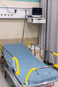 Close-up of an empty hospital bed with safety rails and a modern vital signs monitor in a clean, medical room setting