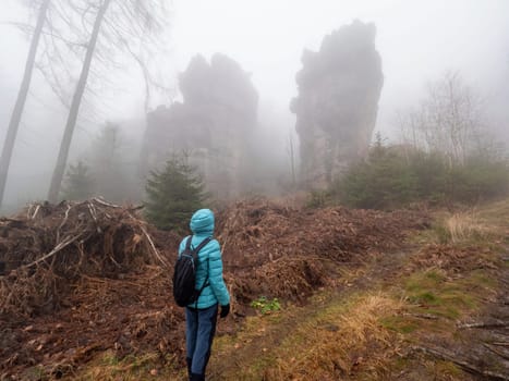 Women backpacker in blue warm jacket wathichng to rocks in heavy mist. Winter misty walk