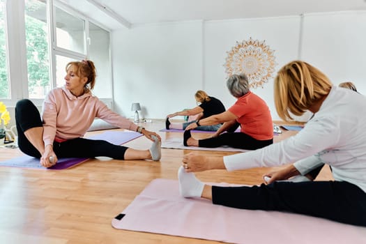 A group of senior women engage in various yoga exercises, including neck, back, and leg stretches, under the guidance of a trainer in a sunlit space, promoting well-being and harmony.