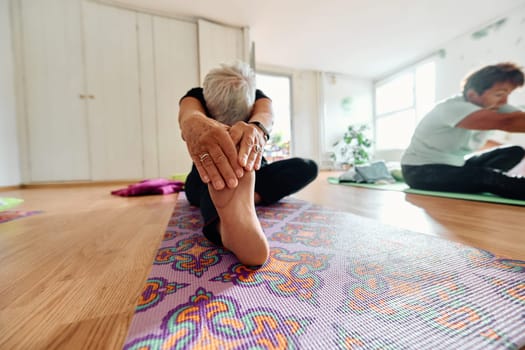 An elderly woman gracefully engages in various yoga poses, stretching her limbs and finding serenity in a modern sunlit space under the guidance of a trained instructor, embodying the essence of active and mindful aging.