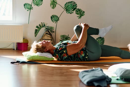 In a sunlit space, a senior woman gracefully practices rejuvenating yoga, focusing on neck, back, and leg stretches, embodying serenity and well-being.