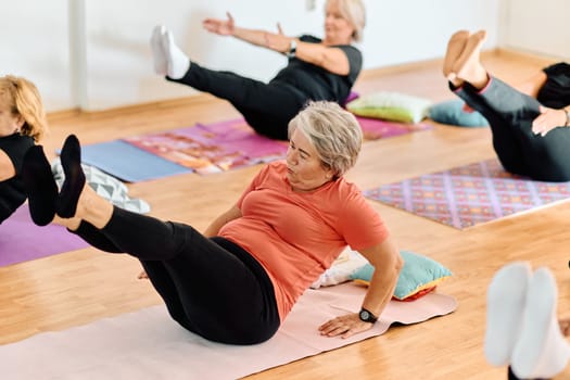 A group of senior women engage in various yoga exercises, including neck, back, and leg stretches, under the guidance of a trainer in a sunlit space, promoting well-being and harmony.