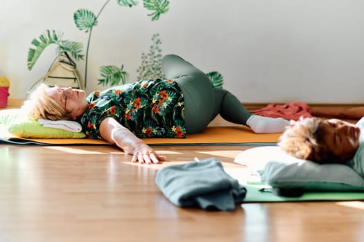 A group of senior women engage in various yoga exercises, including neck, back, and leg stretches, under the guidance of a trainer in a sunlit space, promoting well-being and harmony.