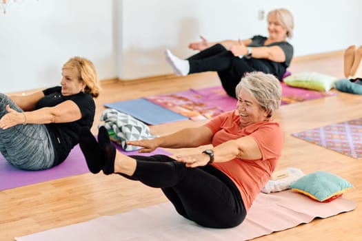 A group of senior women engage in various yoga exercises, including neck, back, and leg stretches, under the guidance of a trainer in a sunlit space, promoting well-being and harmony.