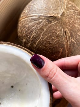 A woman's hand bordeaux dark red manicure on the background a half of a coconut. High quality photo