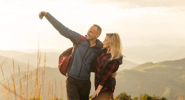 A man and a woman in tourist equipment are standing on a rock and admiring the panoramic view. A couple in love on a rock admires the beautiful views. A couple in love is traveling. A couple on a hike