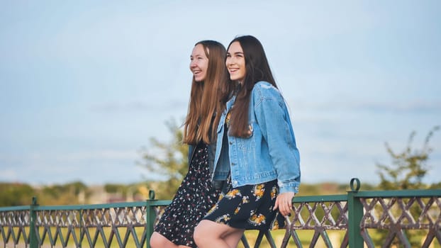 Two girlfriends talking sitting on the fence