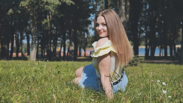 A beautiful girl poses sitting in the park on the grass