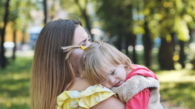 A mother hugs her young daughter in the park in the summer