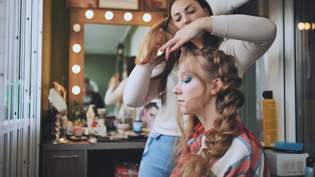 The girl makeup artist makes a braid for the model