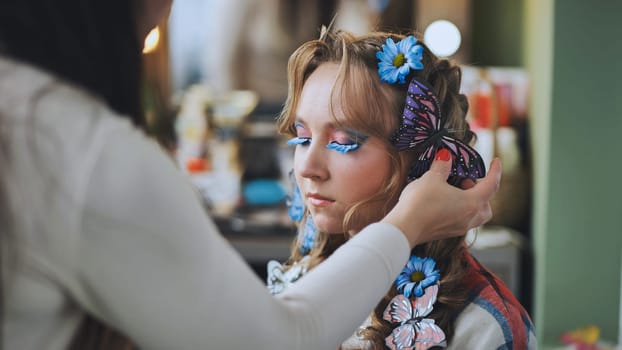 The hairdresser decorates the model's hair with blue flowers and butterflies