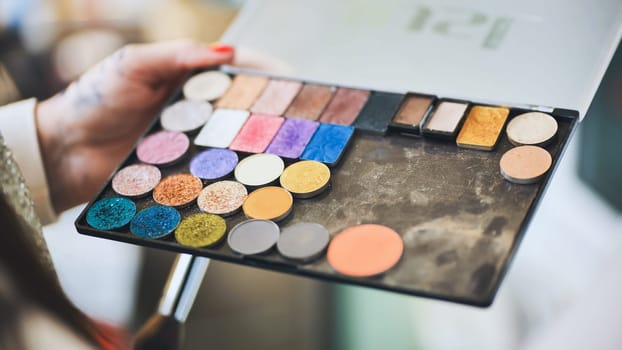 The makeup artist is holding a palette of shadows