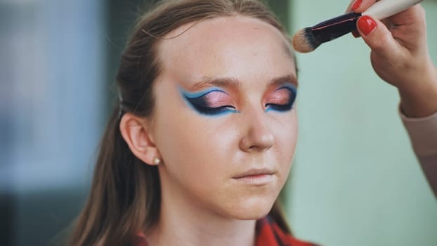 The makeup artist powders the face of the model