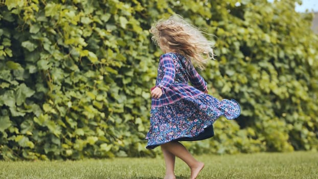 A little girl in a dress twirls in the garden