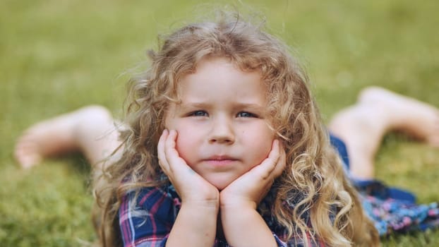 A little curly-haired girl lies on the grass in the garden