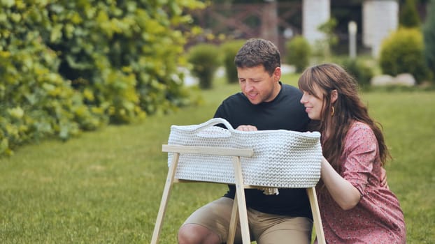 A young couple looks at their newborn baby in a cradle in the garden